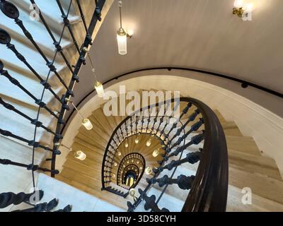 Wendeltreppe, kunstvolles Geländer, warme Pendelleuchten, kreisförmiges Design, dramatische Innenausstattung Stockfoto