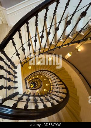Wendeltreppe von oben mit schmiedeeisernem Geländer, Holztreppen und warmen Pendelleuchten schaffen eine einladende Innenatmosphäre Stockfoto