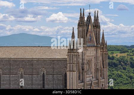 Italien - Orvieto - Kathedrale von Orvieto - gotische Fassade mit Türmen und gestreiftem Kirchenschiff, das sich über bewaldeten Hügeln des Moro-Turms erhebt Stockfoto