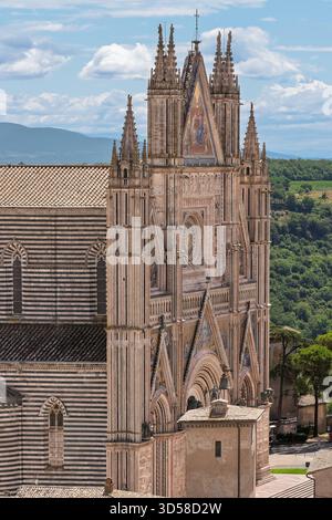 Italien - Orvieto - Duomo di Orvieto - gotische Fassade mit Mosaiken, Rosenfenster und Türmen über dem gestreiften Kirchenschiff mit Blick auf die umbrischen Hügel Stockfoto