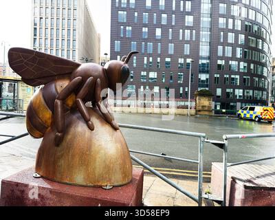 Manchester, Großbritannien - 4. Oktober 2025: Eine große Skulptur aus rostigen Bienen neben einem Geländer entlang eines Flusses, Stadtbild mit modernen Gebäuden. Stockfoto