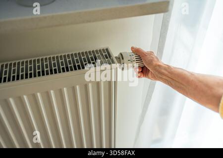 Ältere Frau, die die Heizung an einem Heizkörper in ihrem Haus anpasst, Nahaufnahme Stockfoto