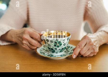 Die Hände der Seniorin halten eine Tasse Tee auf dem Tisch, Nahaufnahme Stockfoto