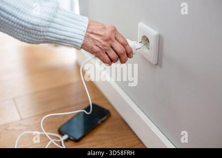 Nahaufnahme einer älteren Frau, die einen Netzstecker in eine Steckdose steckte, um ihr Telefon aufzuladen Stockfoto