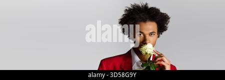 Ein junger, schmetternder Herr, gekleidet in einem scharfen Anzug, posiert elegant und hält eine weiße Rose. Stockfoto