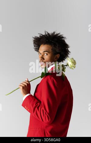 Ein junger Mann mit stilvollem, elegant gekleidetem Haar blickt zurück, während er eine Rose mit Selbstvertrauen hält. Stockfoto