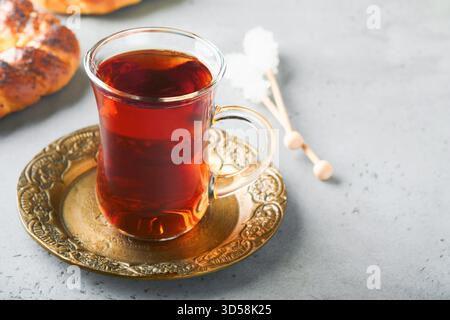 Türkischer schwarzer Tee. Eine Glasschale türkischer schwarzer Tee und knuspriger türkischer traditioneller Bagel auf grauem Betontischhintergrund. Frühstücksgebäck-Konzept. Traditionelles türkisches Heißgetränk. Stockfoto