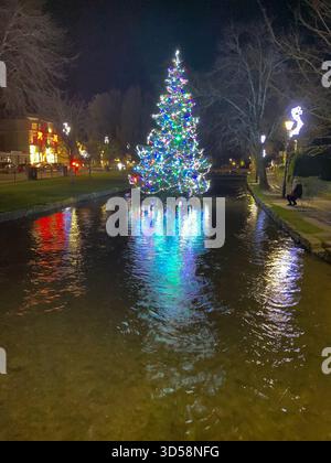 Ein Weihnachtsbaum in Bouton-on-the-Water steht inmitten des flachen Flusses Windrush, der wegen seiner „Venedig der Cotswolds“ genannt wird Stockfoto