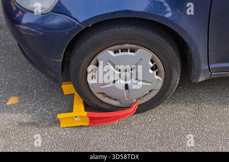 Nahaufnahme einer gelben und roten Radklammer, die um den Reifen eines blauen Autos befestigt ist, was auf ein Parken oder einen Verstoß gegen die Zulassung hinweist. Utrecht Niederlande Stockfoto