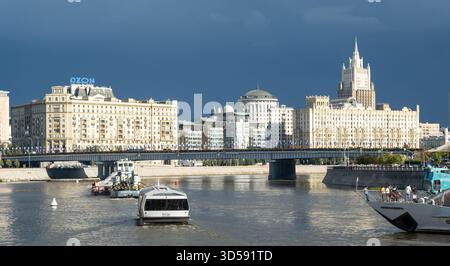 25. August 2025, Moskau, Russland. Der Fluss Moscows reflektiert markante Gebäude, wobei Boote unter einem bewölkten Himmel über dem Wasser navigieren, was die ci hervorhebt Stockfoto
