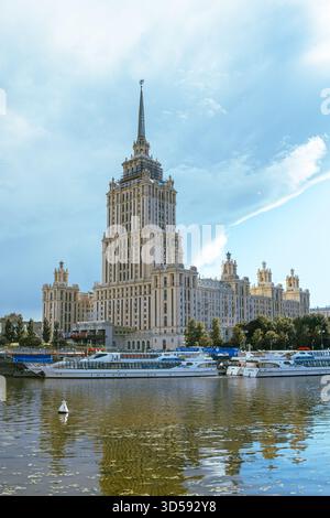 25. August 2025, Moskau, Russland. Ein atemberaubender Wolkenkratzer steht hoch am Fluss und spiegelt seine Pracht auf dem Wasser wider, während die Boote friedlich gleiten Stockfoto