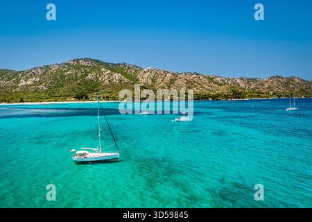 Eine ruhige Küstenszene mit weißen Segelbooten, die in kristallklarem türkisfarbenem Wasser ankern, Korsika, Frankreich Stockfoto