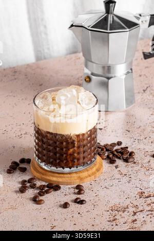 Eiskaffee in ein Glas mit Mokakanne auf beigefarbenem Küchentisch Stockfoto