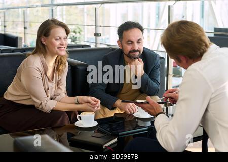 Kaukasische junge Frau und junger Mann aus dem Nahen Osten sitzen am Tisch und lauschen dem kaukasischen Mann mittleren Alters, der Informationen erklärt Stockfoto