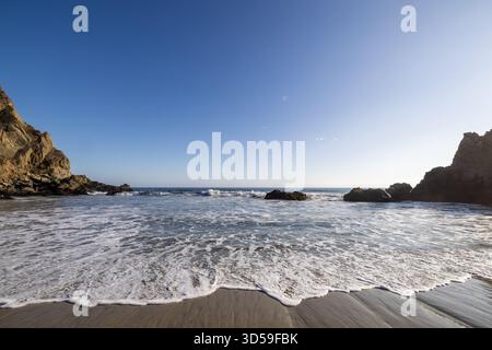 Schäumende einfallende Brandung, die über nassem Sand in Richtung felsiger Küste am Pfeiffer Beach, Big Sur, Kalifornien, fließt. Stockfoto