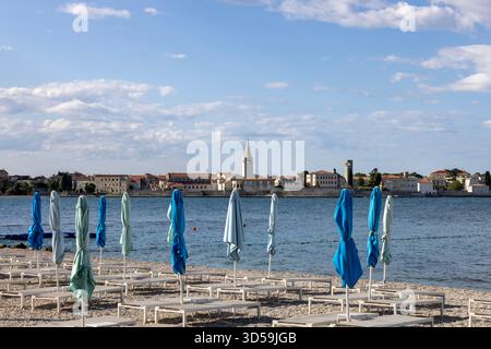 Porec, Kroatien, Istrien - 30. September 2023: Blick vom Strand mit Sonnenschirmen und Liegestühlen auf die Stadt mit dem Glockenturm der Basilika Euphrasian Stockfoto
