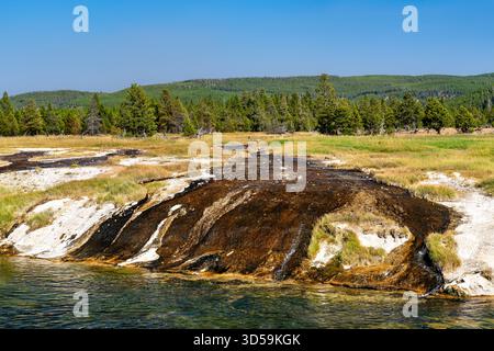 Dunkle Bakterienmatten fließen über eine weiße Sinterkruste in den Firehole River im Lower Geyser Basin des Yellowstone National Park Stockfoto