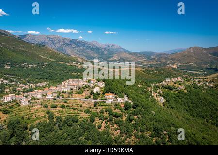 Erhöhter Blick auf ein Bergdorf eingebettet zwischen terrassenförmig angelegten Hügeln, umgeben von grünen Wäldern und Feldern. Korsika, Frankreich Stockfoto