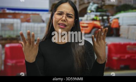 Frau spreizt ihre Hände und zeigt frustrierten Ausdruck in einer Bauszene, während der junge hispanic latin Influencer Emotionen in einem Outdoor-si ausdrückt Stockfoto