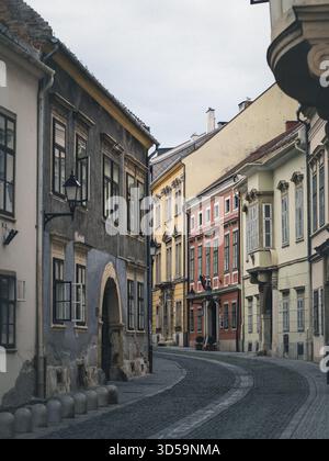 Eine gewundene Kopfsteinpflasterstraße in Sopron, Ungarn, ist gesäumt von bunten barocken und neoklassizistischen Gebäuden, verwitterten Fassaden und altem Charme Stockfoto
