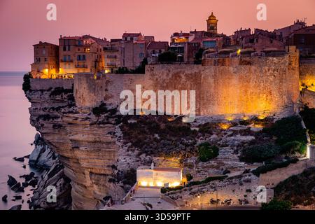 Ein dramatischer Sonnenuntergang taucht eine mittelalterliche Festung an den Klippen und eine lebhafte Küstenstadt in warmes Licht, Korsika, Frankreich Stockfoto