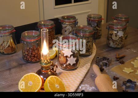 Hausgemachte Weihnachtskekse und Nüsse in Glasgläsern mit einer alten Öllampe und frischen Orangen auf einem rustikalen Holztisch. Stockfoto