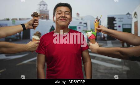 Junger Mann in einem roten Hemd Augen geschlossen lächelnd, während vier Hände Eiskegel auf einer Straße in der Nähe von weißen Gebäuden anbieten; Freudenverführung. Stockfoto