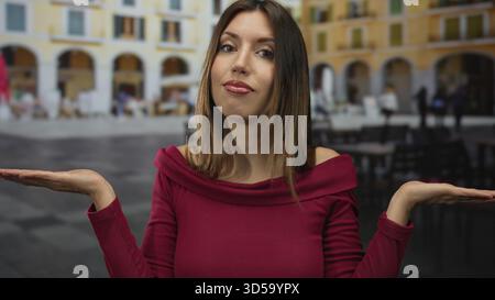 Die junge hispanische Frau in rotem Oberteil hält die Handflächen auf der belebten Straße neben verschwommenen Kaffeetischen hoch; Zweifel. Stockfoto