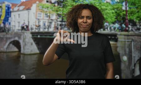 Frau zeigt auf einer amsterdamer Straße an einer Kanalbrücke mit Fahrrädern und Bäumen die Daumen nach unten; Kritik an der Missbilligung. Stockfoto