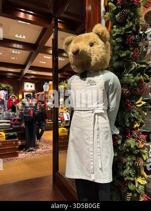 London, Großbritannien, 20. November 2025 Eine große Teddypuppe mit grauer Schürze und gestreiftem Hemd steht neben einer weihnachtsgirlande in üppiger Dekora Stockfoto