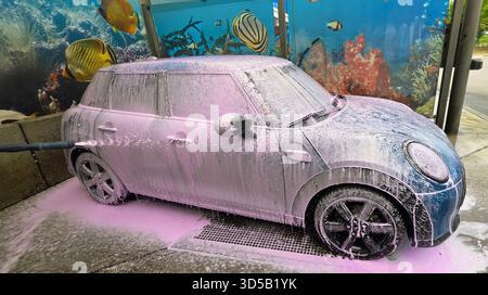 Berlin, Deutschland - 18. Mai 2025: Mini Cooper wird mit Schaum in einer Autowaschanlage mit Unterwasser-Wandgemälde gewaschen. Stockfoto