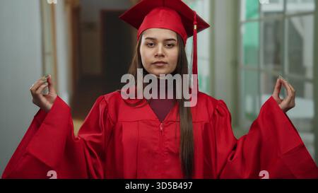 Junge Frau in rotem Abschlusskleid, die im Hotelflur meditiert, symbolisiert Ruhe und Leistung drinnen. Stockfoto