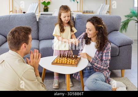 Glückliche Familie, die Tochter beibringt, gemeinsam Schach auf dem Wohnzimmerboden zu spielen Stockfoto