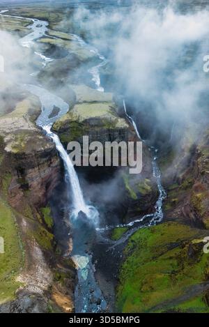 Ein atemberaubender Blick auf den Haifoss-Wasserfall, der von hohen Klippen in einen ruhigen Fluss unter Island stürzt Stockfoto