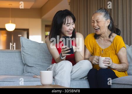 Asiatische ältere Mutter und Tochter lachen zusammen auf dem Sofa, während sie auf das Smartphone schauen Stockfoto