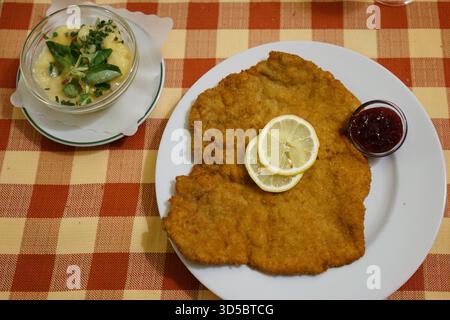 Traditionelles Wiener Schnitzel serviert mit Kartoffelsalat und Preiselbeermarmelade auf einem Teller. Stockfoto