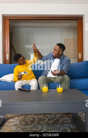 Afroamerikanischer Vater und Sohn haben sich beim Spielen von Videospielen zu Hause High Five gemacht Stockfoto