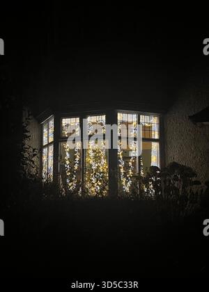Traditionelle Erkerfenster, dekoriert mit warmweißen Lichterketten, die bei Dämmerung in einem Wohnhaus in Hull, England, leuchten. Gemütlicher Winterurlaub Stockfoto