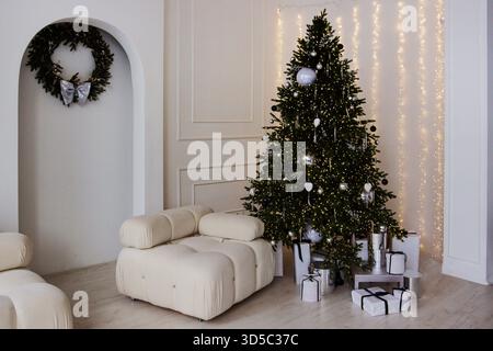 Ein wunderschöner Weihnachtsbaum mit Kugeln und anderen Dekorationen, Geschenkboxen unter dem Baum, Wohnzimmereinrichtung, Polstermöbel. Stockfoto