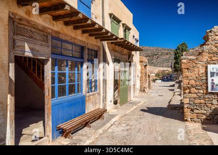 Alter Innenhof auf der Insel Spinalonga mit bunten Holztüren, Steinmauern und Bergkulisse an der Küste Kretas. Stockfoto