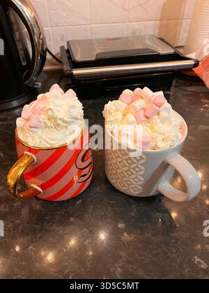 Zwei Keramikbecher gefüllt mit reichhaltiger heißer Schokolade, garniert mit Schlagsahne und Marshmallows auf einer Küchentheke für eine festliche Winterstimmung Stockfoto