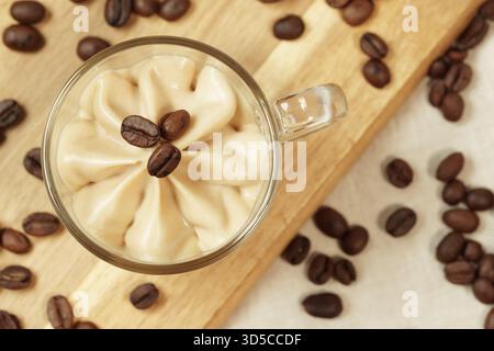 Kalter Kaffee Creme Milchshake Dessert in einem Glas mit Kaffeebohnen auf einem hölzernen Schneidebrett von oben aus Nahaufnahme. Stockfoto
