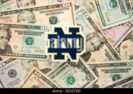 KIEW, UKRAINE - 23. FEBRUAR 2025 Notre Dame Fighting Irish Basketball Team Badge liegt auf einer großen Menge von US-Dollar-Scheinen Stockfoto
