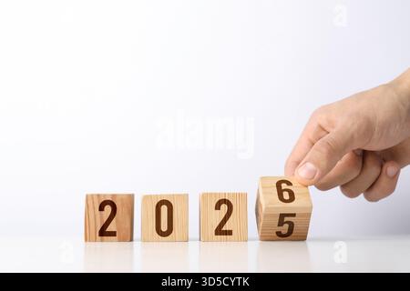 Neujahr. Mann dreht den Würfel mit den Zahlen 5 und 6 um 2026 auf hellem Hintergrund zu machen, Nahaufnahme Stockfoto