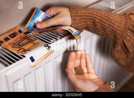 Ein Mädchen in einem Pullover zählt Geld an einem Heizkörper: 50 und 20 Euro-Scheine, 20 Euro Nahaufnahme und 50 Euro-Cent in den Fingern. Das Zimmer ist kalt, hoch Stockfoto
