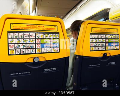 Manchester, Großbritannien - 04. Oktober 2025: Passagiere in einer gelben Flugzeugkabine sehen Sicherheitsdiagramme auf den Rückenlehnen in Manchester. Stockfoto