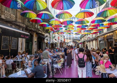 Rosa Straße Lissabon, offiziell Rua Nova do Carvalho genannt, Straße mit rosa Pflaster und mehrfarbigen Regenschirmen, die darüber hängen, Portugal, Europa Stockfoto