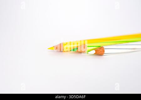 Eine Nahaufnahme der geschärften Spitzen gelber, grüner und weißer Bleistifte vor einem hellweißen Hintergrund. Stockfoto