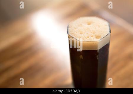 Eine vertikale Nahaufnahme eines Glases mit dunklem, eiskaltem Cold Brew oder Nitrokaffee mit einer dicken Schicht goldenem Schaum/Schaum. Stockfoto