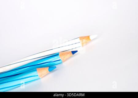 Drei gestreifte Buntstifte in Blau- und Weißtönen liegen schräg auf weißem Hintergrund. Der Fokus liegt auf den geschärften Spitzen. Stockfoto